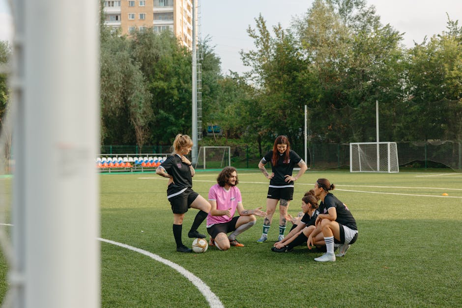 A mixed group of adults gathers on a sunny day for a team discussion on an outdoor football field.